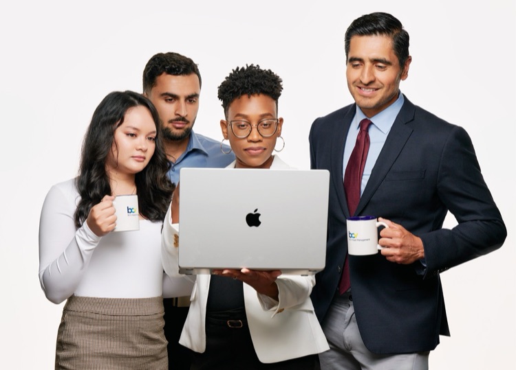 Four colleagues gathered around a laptop with coffee mugs, photographed for their company by ATX Headshots