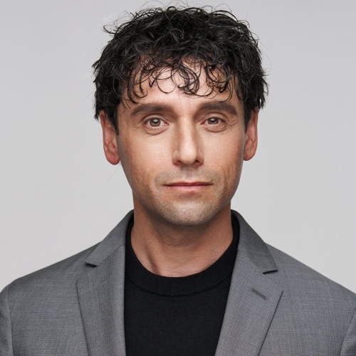 Headshot of a man with curly dark hair in a grey blazer and black t-shirt, ATX Headshots