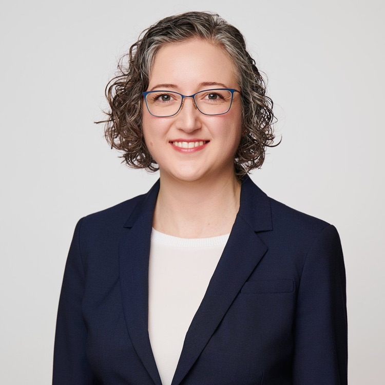 Headshot of a woman in glasses and a navy blazer over a white top, light grey background