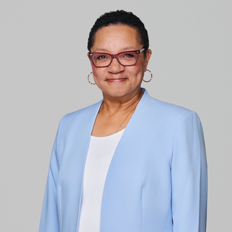 Headshot of a woman in glasses and a pale blue jacket over a white top, light grey background