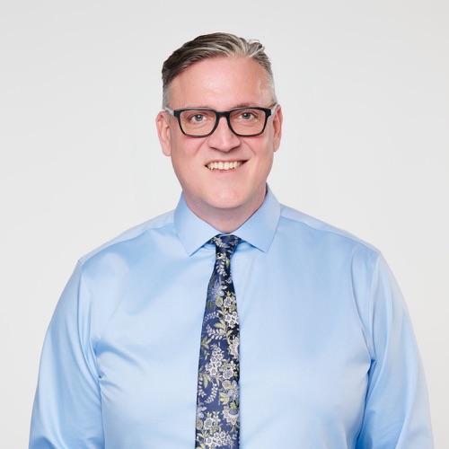Headshot of a smiling man in glasses, a light blue shirt and patterned tie, ATX Headshots