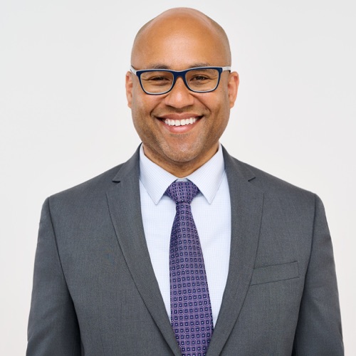 Headshot of a smiling man in glasses, a grey suit and purple tie, ATX Headshots