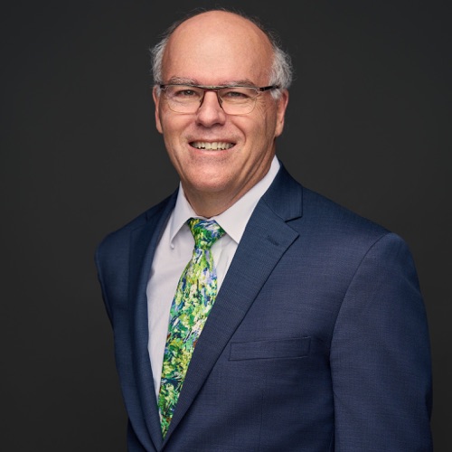 Headshot of a smiling man in glasses, navy suit and green tie, photographed in Cedar Park by Ryan Dunbar
